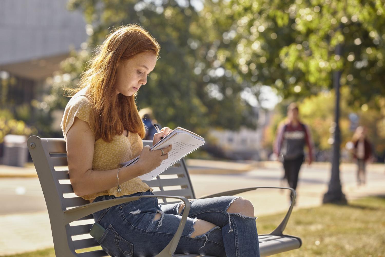 A <a href='http://qkcg.syudia.com'>BETVLCTOR伟德登录</a> student reads on a bench along Campus Drive.